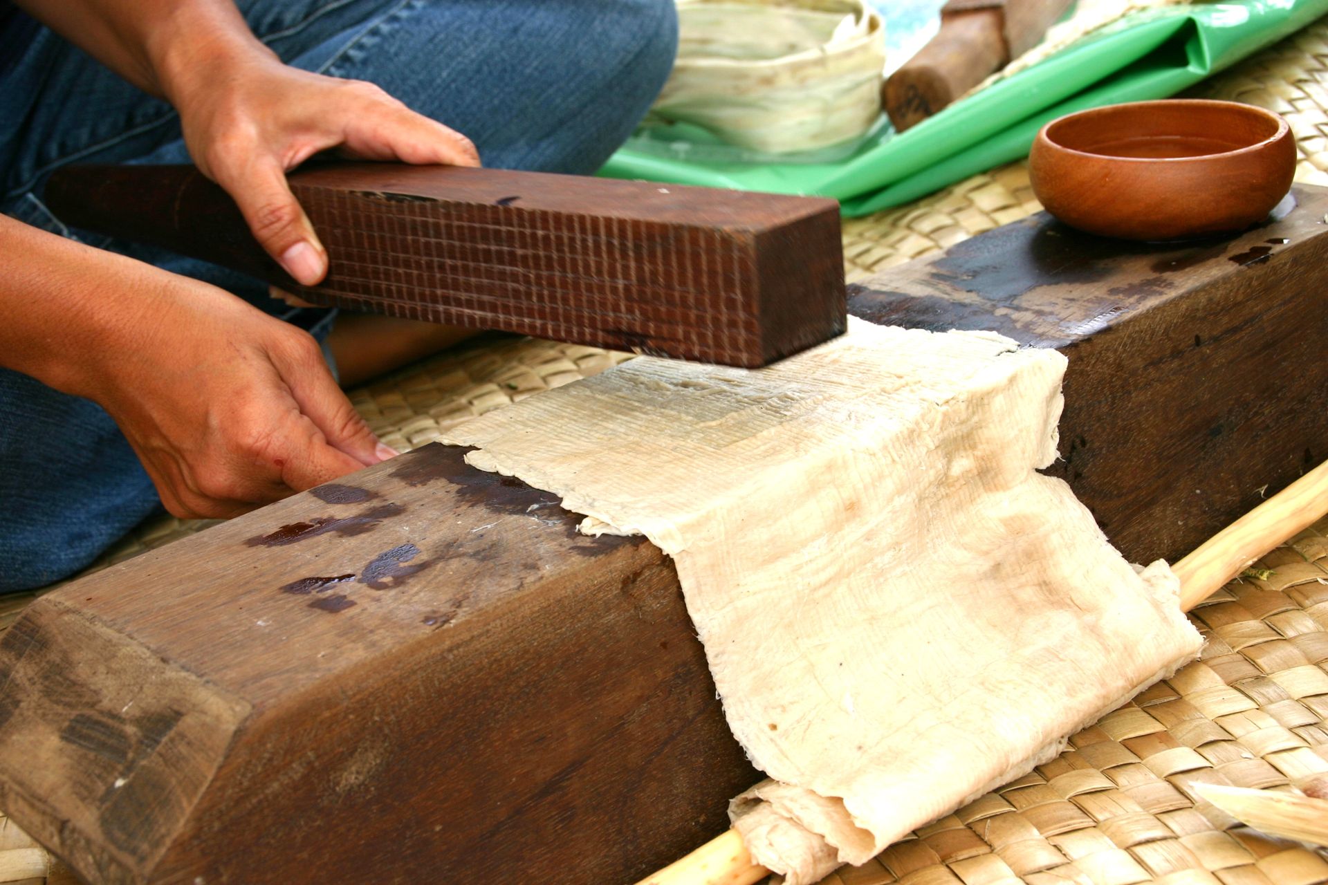 Hands pounding kapa cloth with a wooden beater