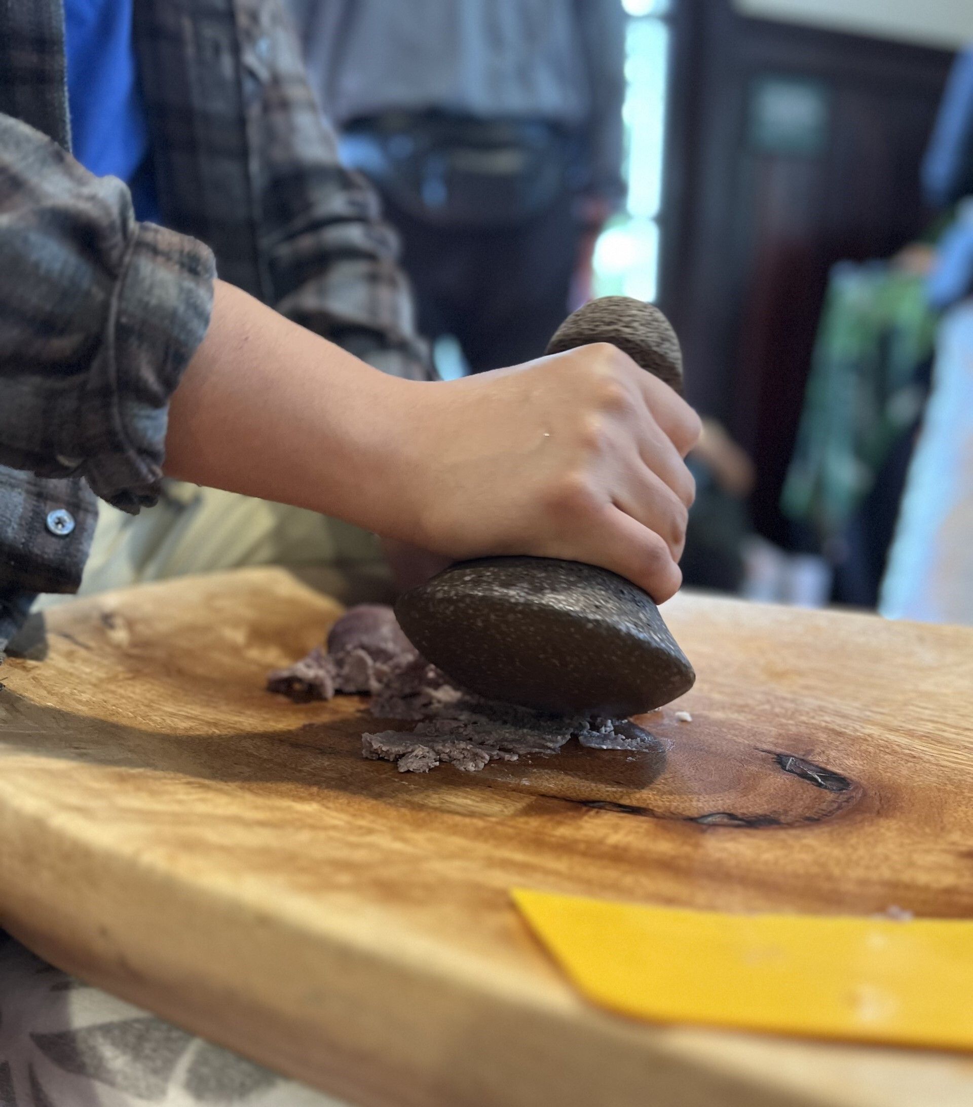Hands pound poi with a stone pounder on a wooden board