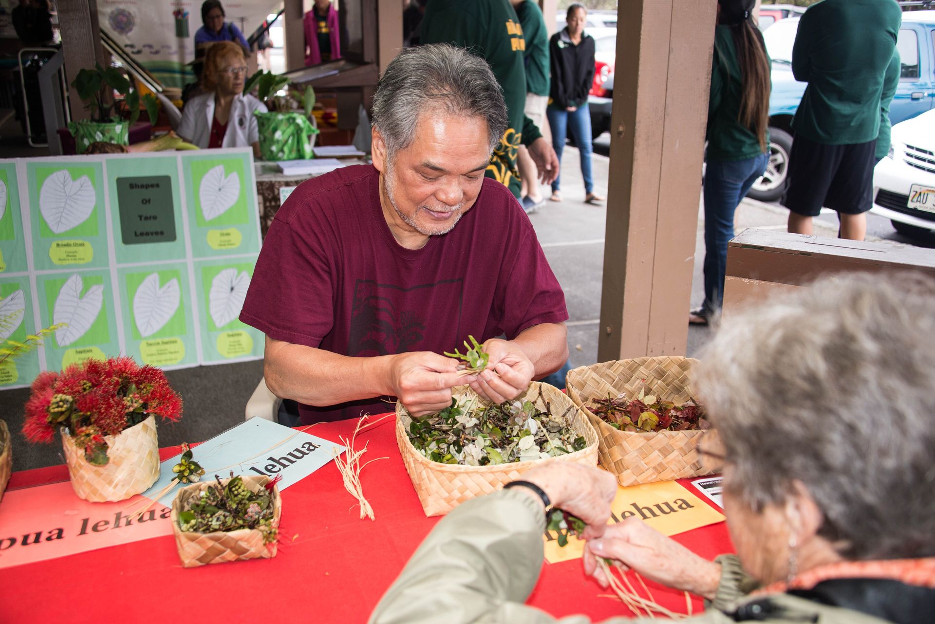 A practitioner demonstrates traditional lei making at a table of flowers